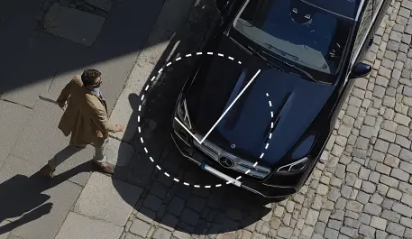 Overhead view of a person walking near a parked black Mercedes-Benz car on a cobblestone street.